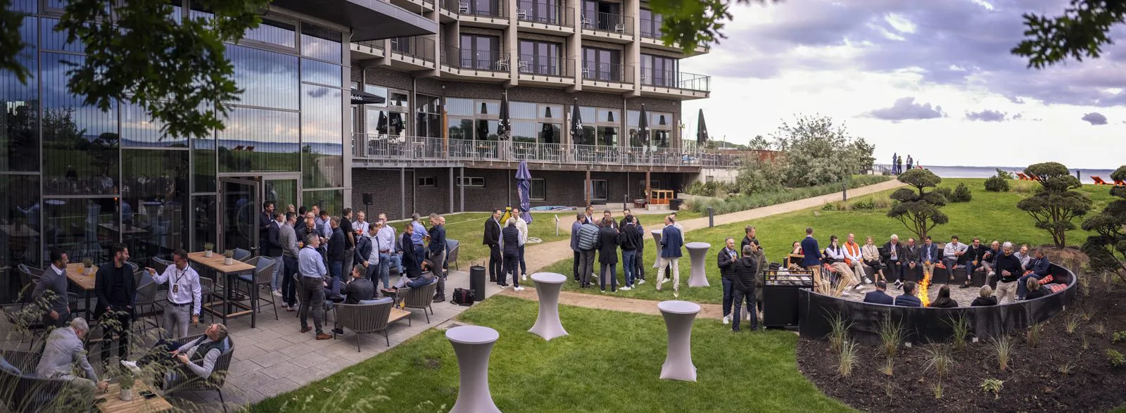Gäste beim Mercedes-Benz-Event auf einer Terrasse mit Stehtischen und Sitzgruppen vor einem Glasgebäude bei Tageslicht.
