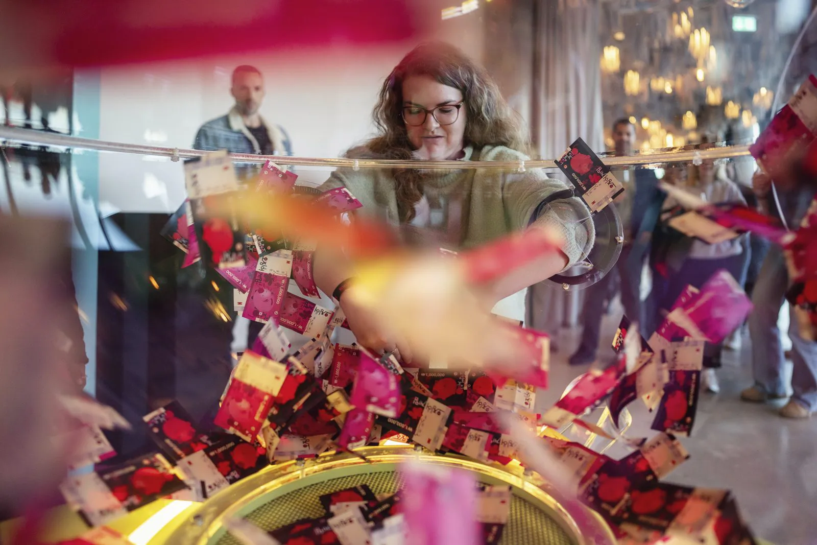 Person mit Brille greift beim Netflix-Event in eine transparente Kabine mit umherwirbelnden bunten Karten.
