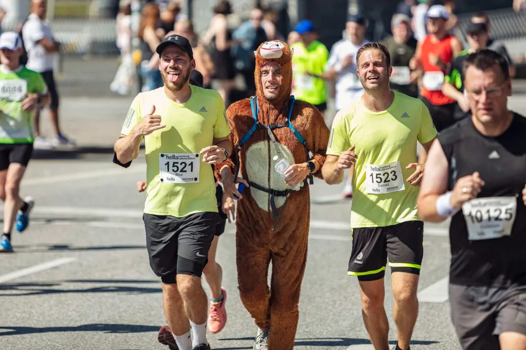 Läufer im Affenkostüm zwischen zwei Läufern in neongelben Shirts auf sonniger Straße beim Halbmarathon.