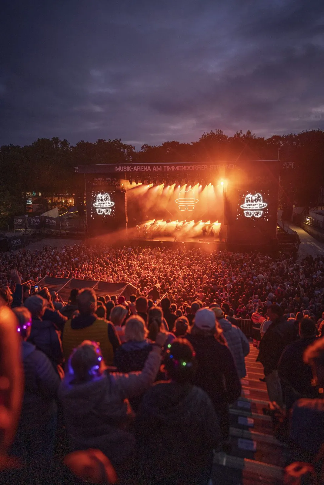 Dichtes Publikum vor einer orange beleuchteten Open-Air-Bühne beim Jan-Delay-Konzert in der Abenddämmerung.