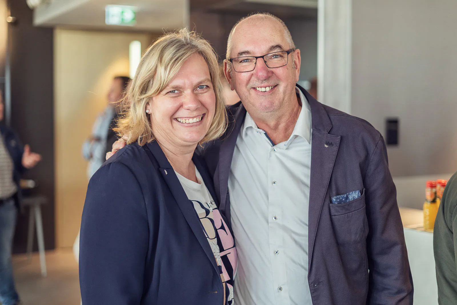 Eine Frau und ein Mann mit Brille stehen lächelnd Arm in Arm im hellen Veranstaltungsraum beim Schüco-Event.
