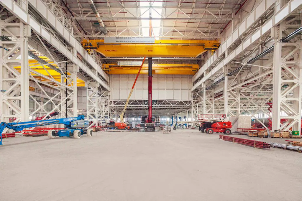 Gelbe Konecranes-Brückenkrane und Hubarbeitsbühnen in einer hohen, lichtdurchfluteten Industriehalle.