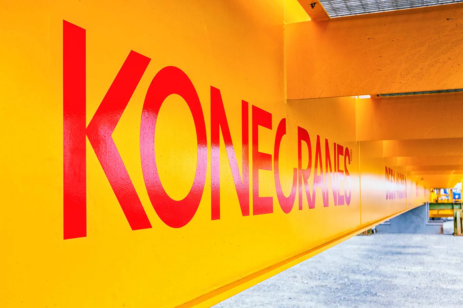 Roter Konecranes-Schriftzug auf einem gelben Kranträger, der sich im Tageslicht über eine Schotterfläche erstreckt.