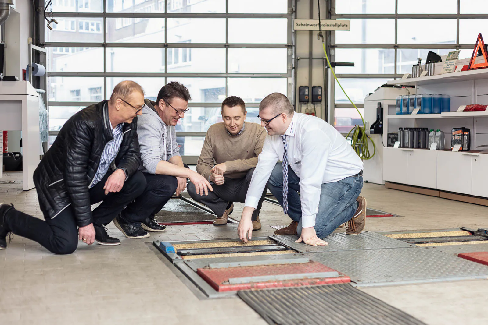 Vier Männer knien in einer hellen VW-Werkstatt und begutachten einen Rollenprüfstand im Boden.