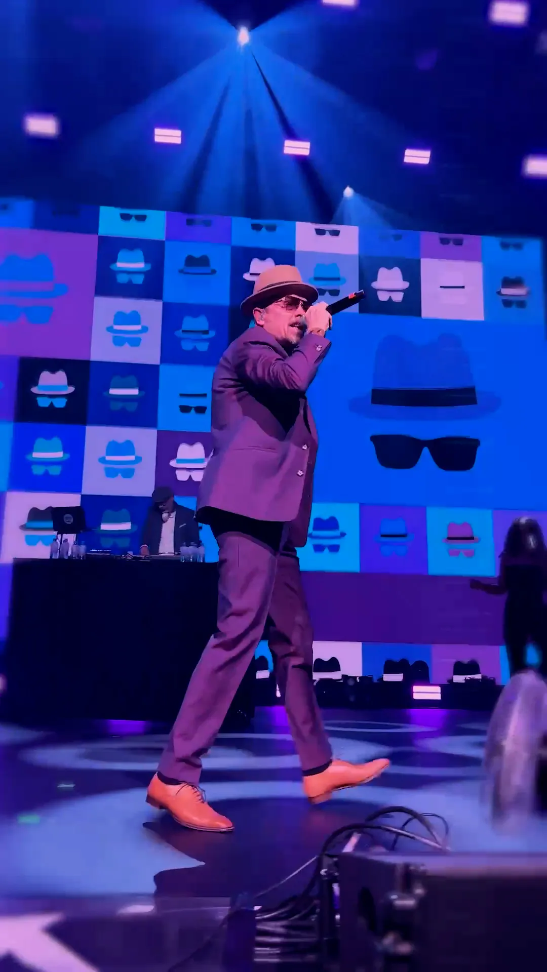 Jan Delay mit Hut und Mikrofon auf einer blau beleuchteten Bühne vor einer Wand mit Logos.