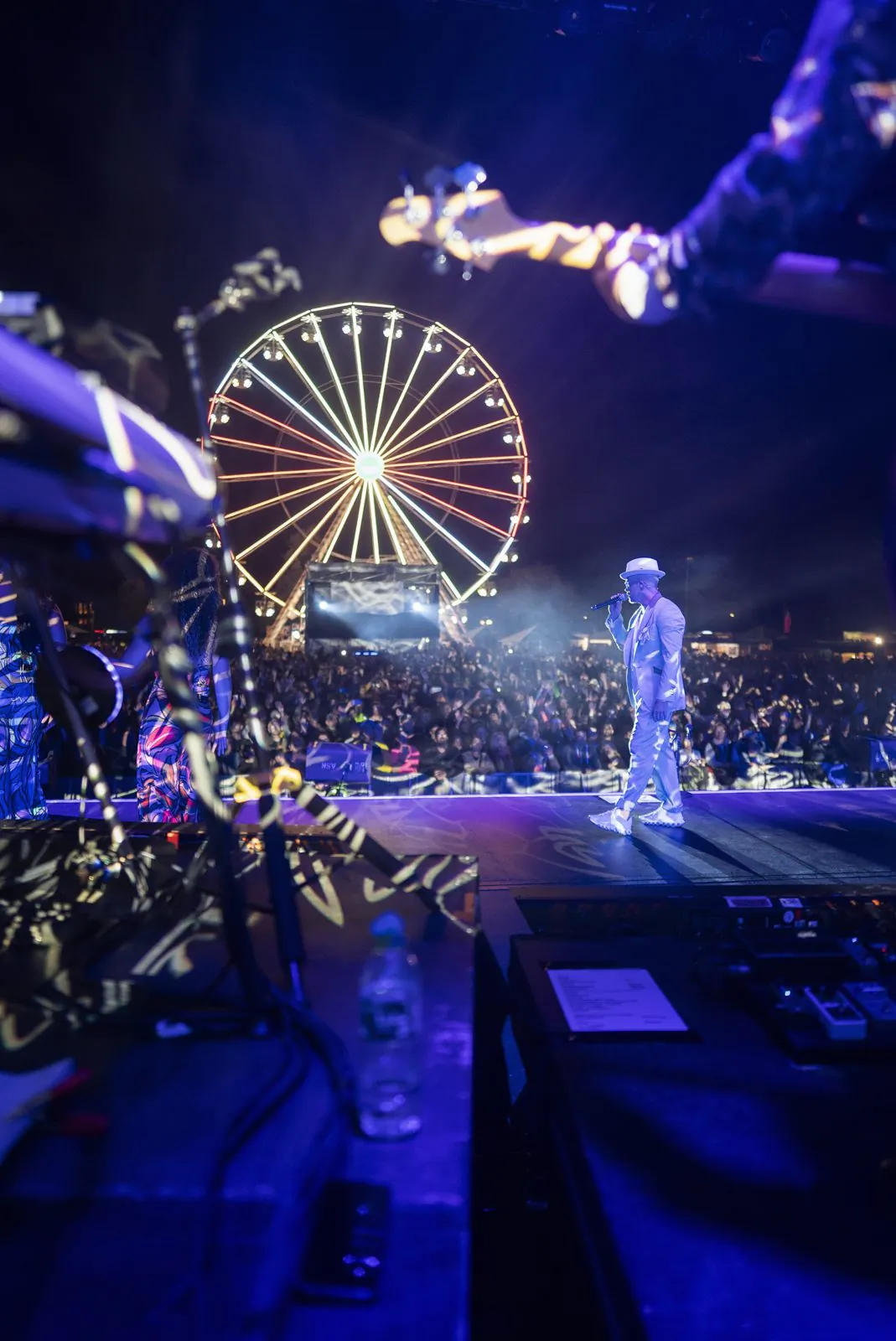 Jan Delay mit Hut und Mikrofon auf blau beleuchteter Open-Air-Bühne, davor Publikum und ein leuchtendes Riesenrad.