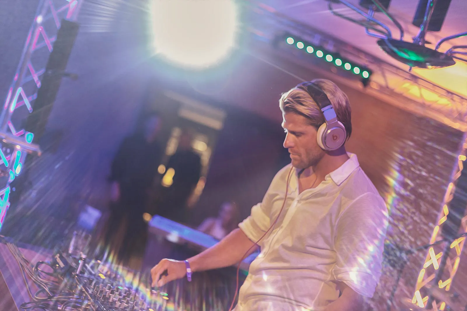 DJ mit Kopfhörern und weißem Hemd bedient ein Mischpult unter buntem Partylicht bei der Sommerparty Aspria.
