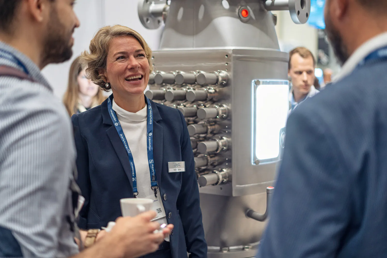 Lächelnde Frau im Gespräch mit zwei Männern vor einer großen Edelstahlmaschine am Messestand von Alfa Laval.