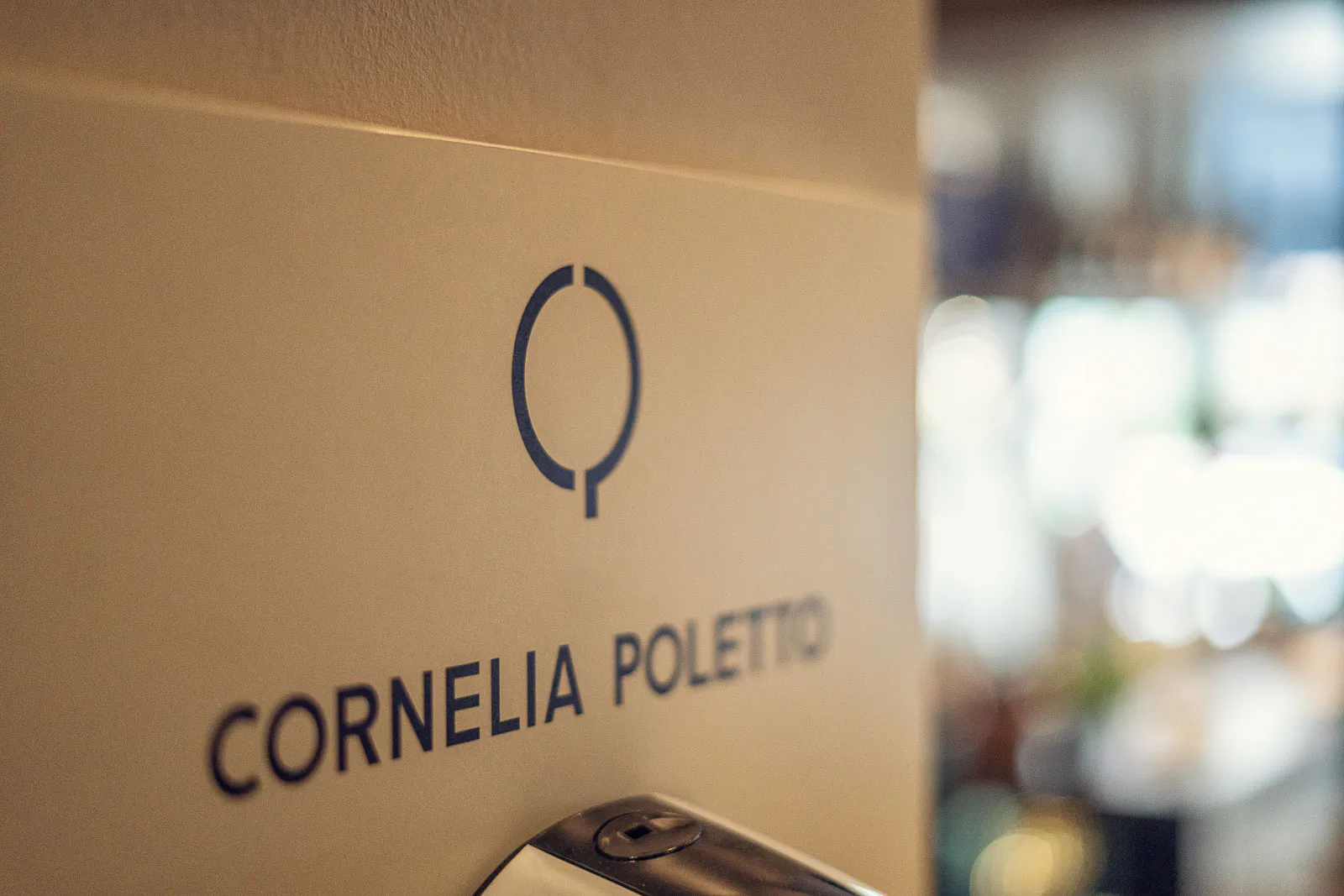 Cornelia-Poletto-Schriftzug mit Logo auf einer warm beleuchteten Wand, dahinter unscharfer Restaurantbereich.