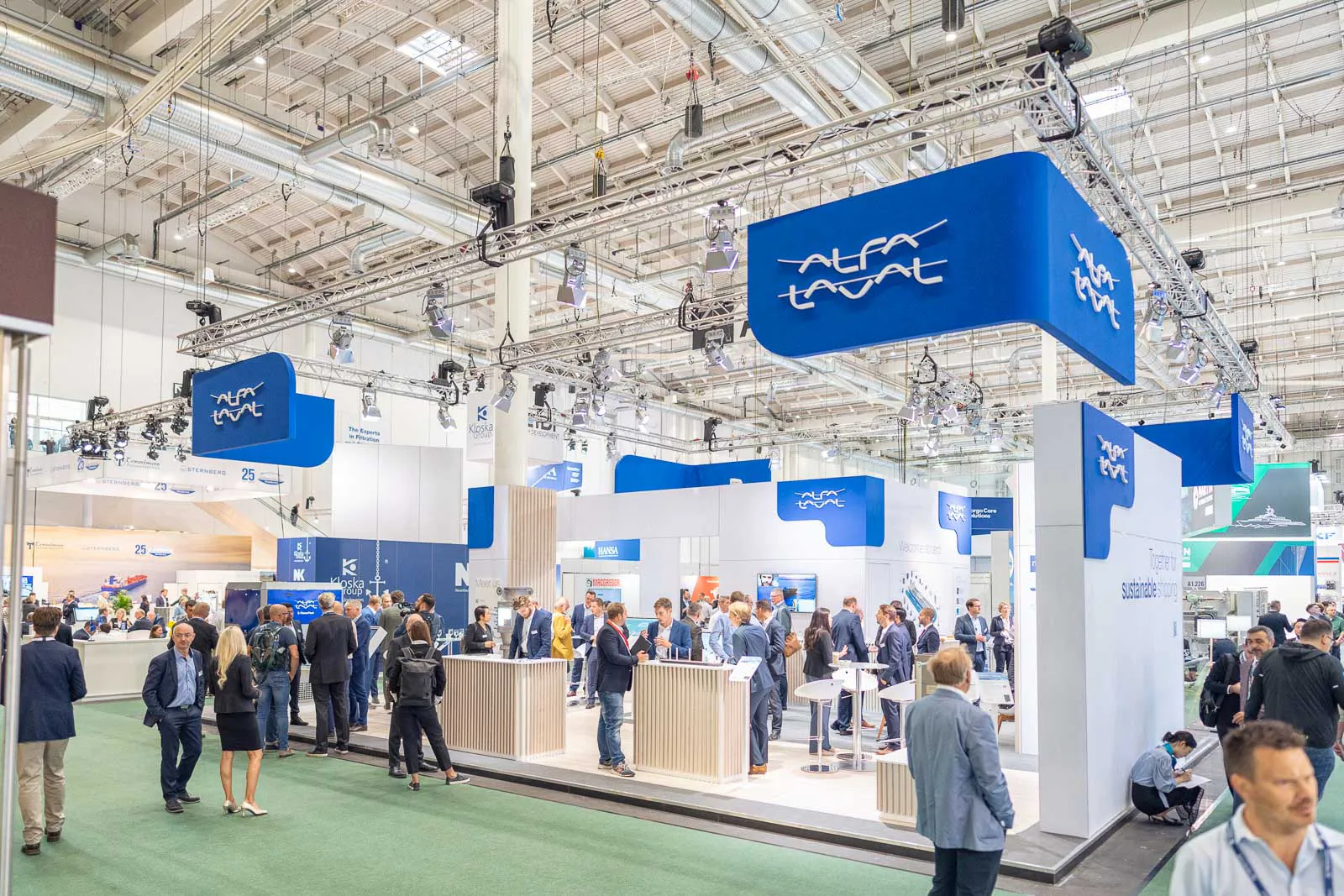 Besucher im Gespräch am hell beleuchteten Alfa-Laval-Messestand mit weißen Theken und blauen Logoschildern.
