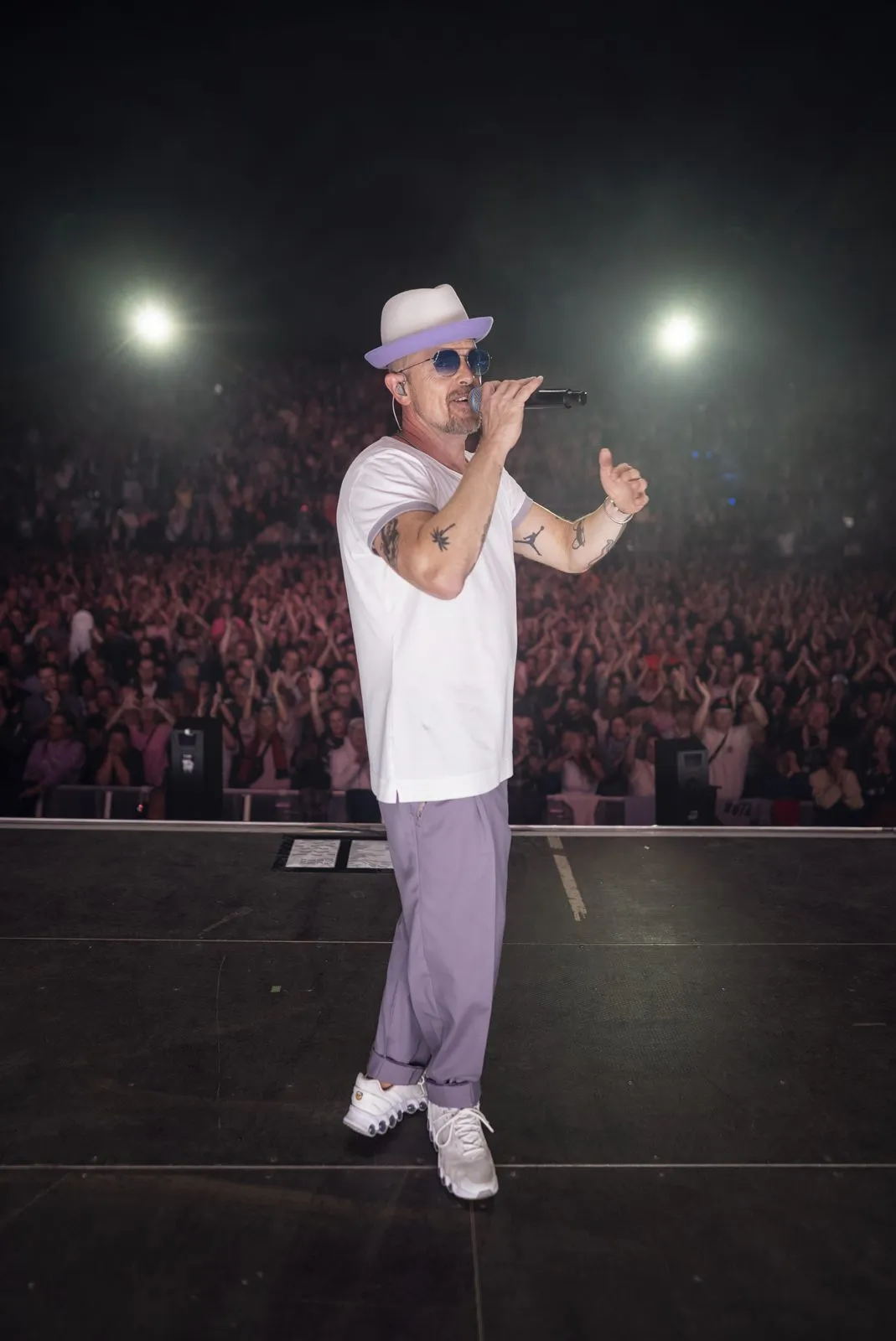 Jan Delay mit Hut und Sonnenbrille singt ins Mikrofon auf einer Bühne vor dichtem Publikum und hellen Scheinwerfern.