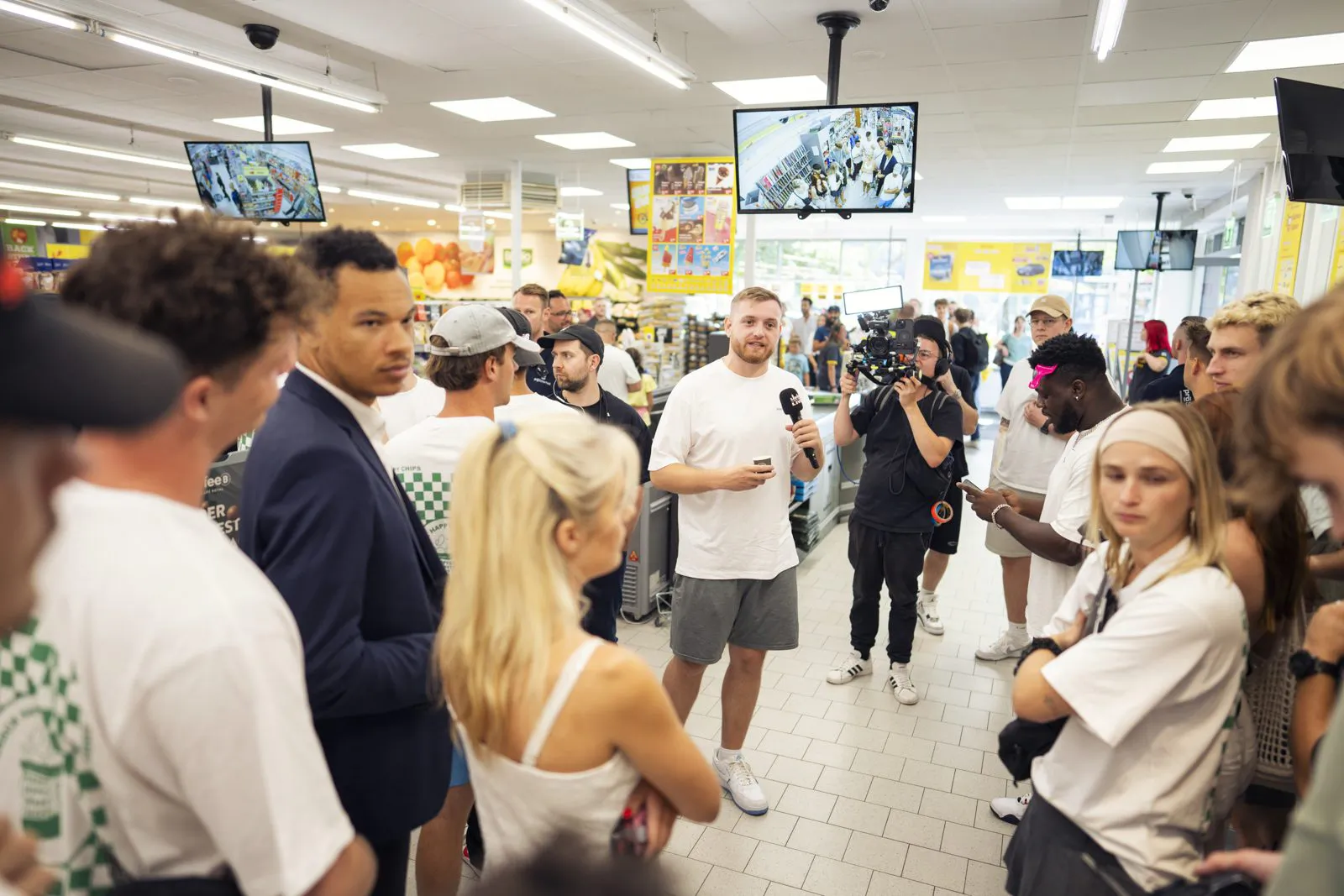 Menschen stehen im hell beleuchteten Netto-Markt um einen Mann mit Mikrofon, ein Kameramann filmt.