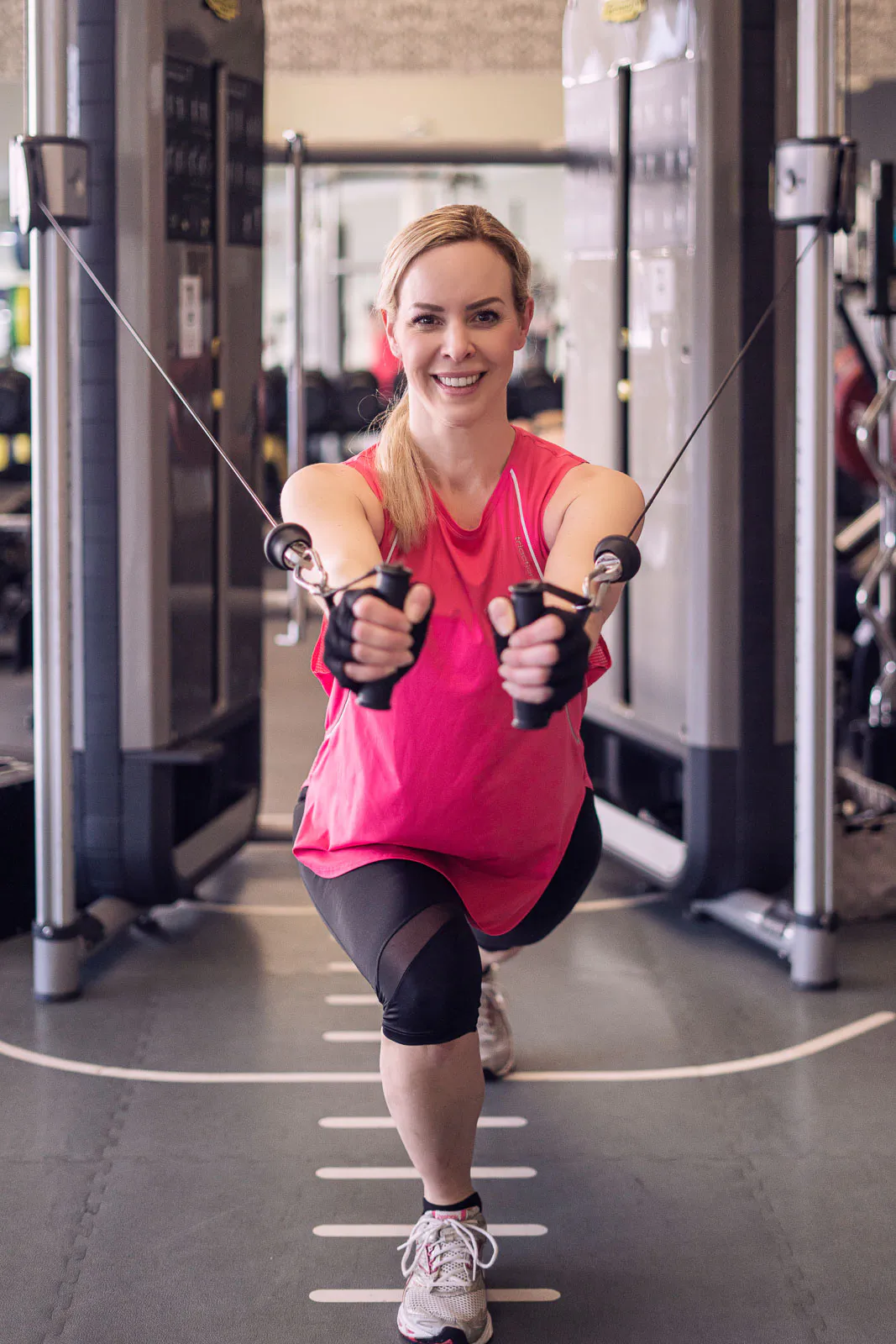 Isabel Edvardsson trainiert lächelnd im pinken Sporttop am Kabelzug im Fitnessstudio.