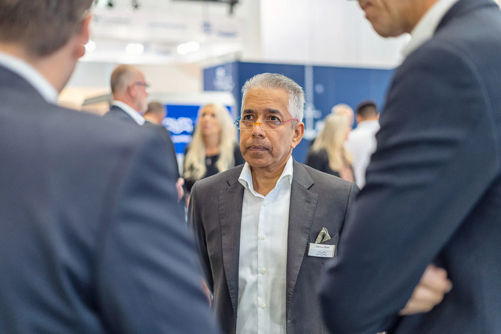 Drei Männer in Anzügen im Gespräch am hell beleuchteten Messestand von Alfa Laval, weitere Besucher im Hintergrund.