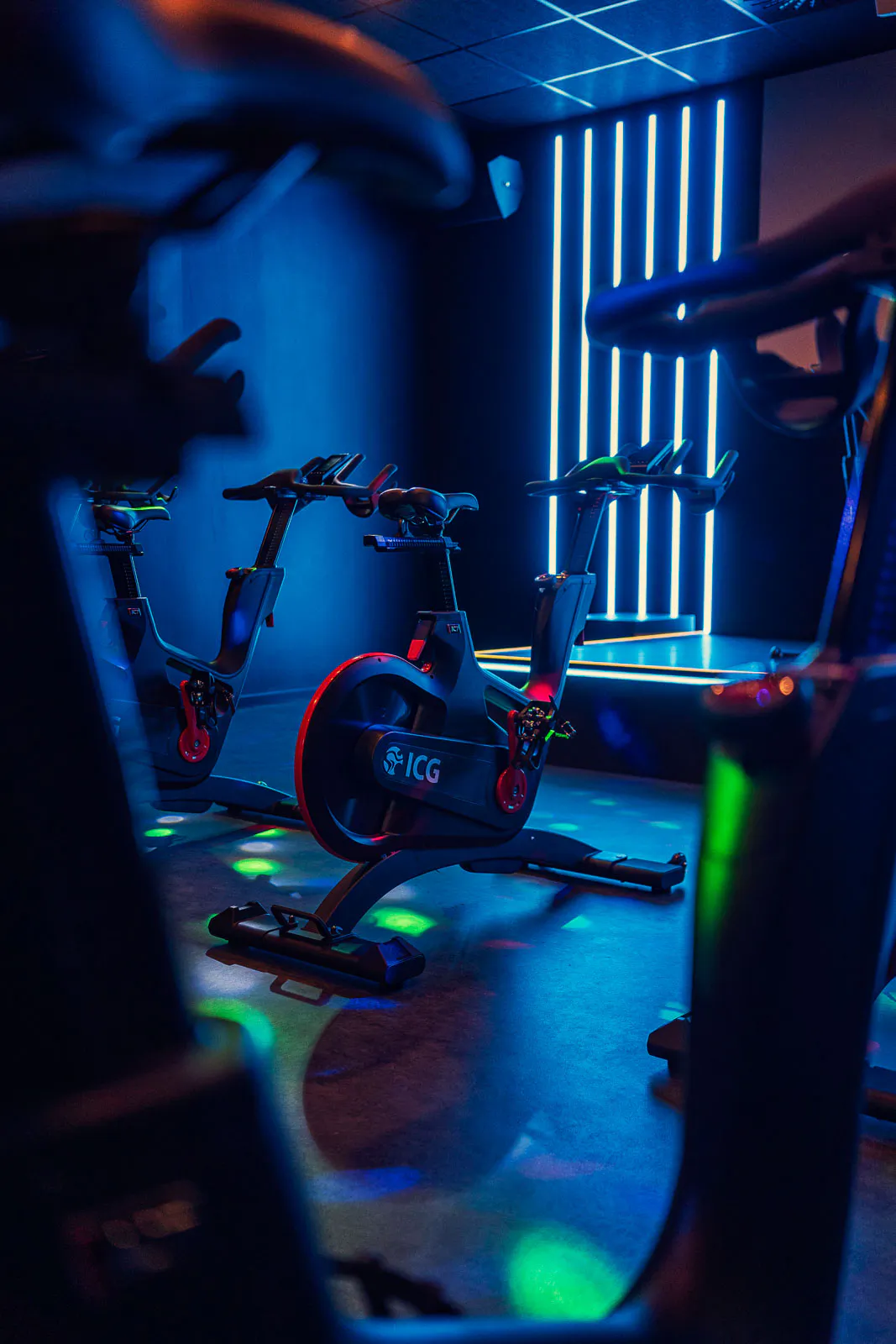 Indoor-Cycling-Räder in einem dunklen Fitnessraum mit blauen Lichtleisten und grünen Lichtpunkten auf dem Boden.