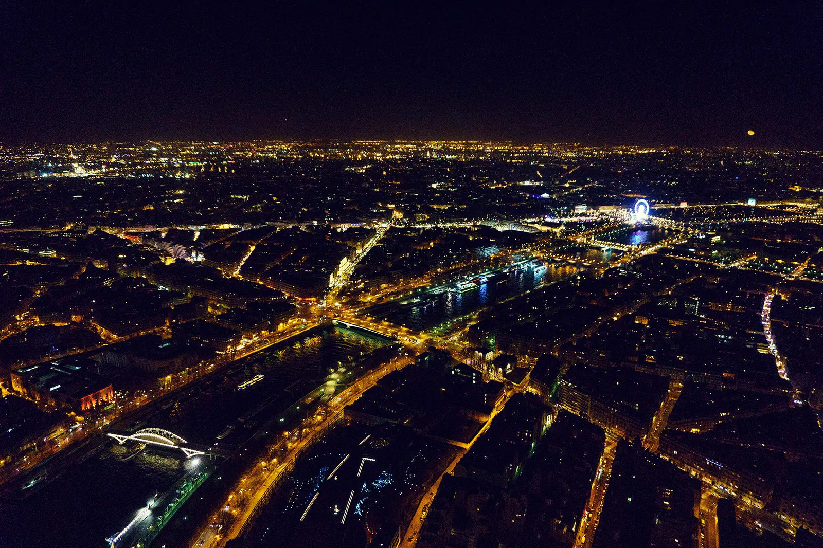 Nächtlicher Blick über Paris mit beleuchteten Straßen, Brücken über die Seine und einem leuchtenden Riesenrad.