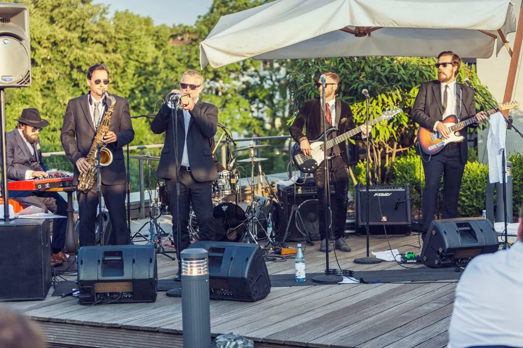 Baba Soul & the Professors of Funk spielen im Sonnenlicht auf einer Holzterrasse unter einem weißen Sonnenschirm.