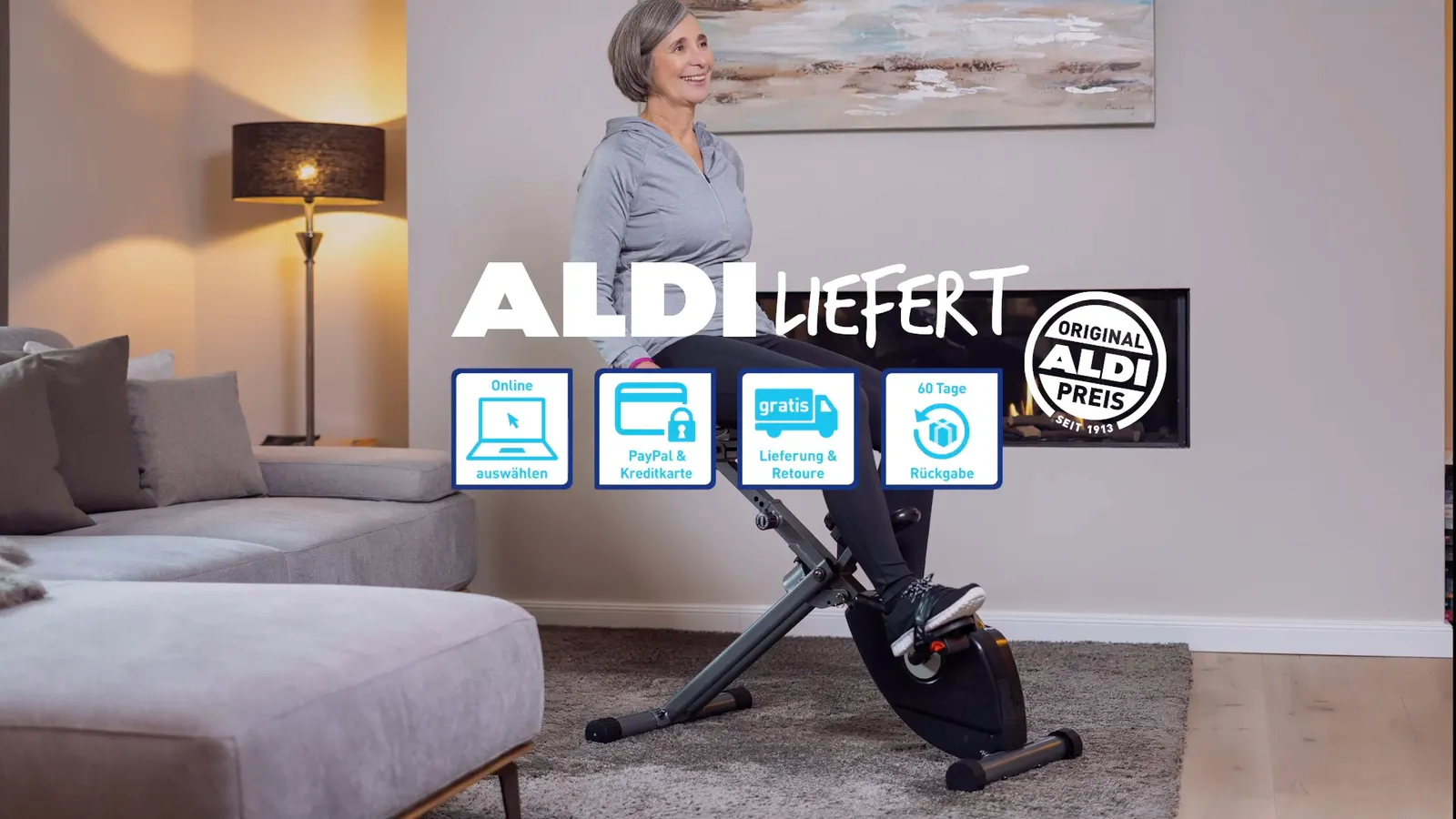 Frau trainiert auf einem Heimtrainer im warm beleuchteten Wohnzimmer, darüber der Werbeschriftzug ALDI LIEFERT.