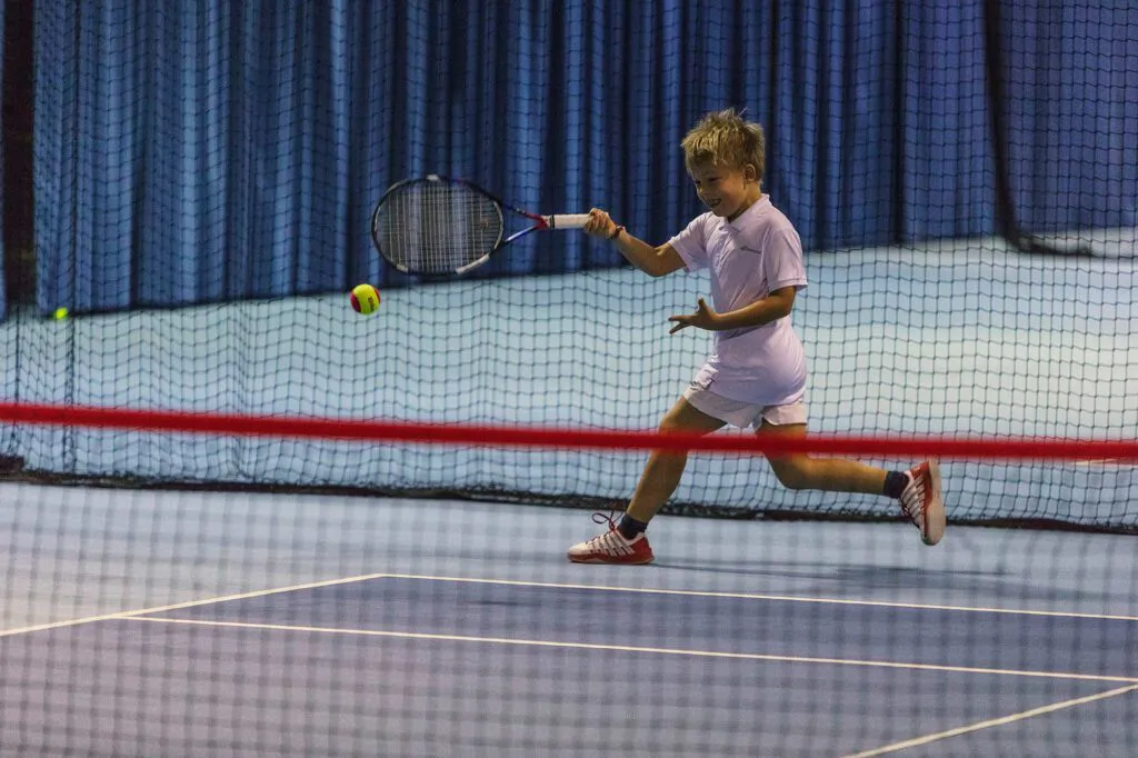 Junger Tennisspieler schlägt beim Wilson Master Cup einen Ball in einer Halle mit blauen Vorhängen.