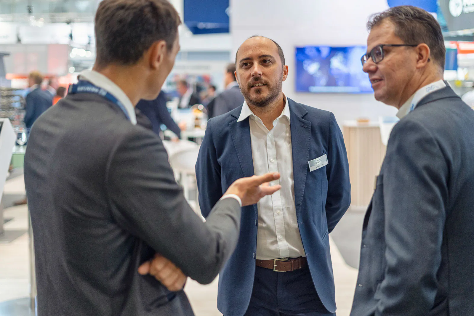 Drei Männer in Anzügen unterhalten sich am hell beleuchteten Messestand von Alfa Laval.