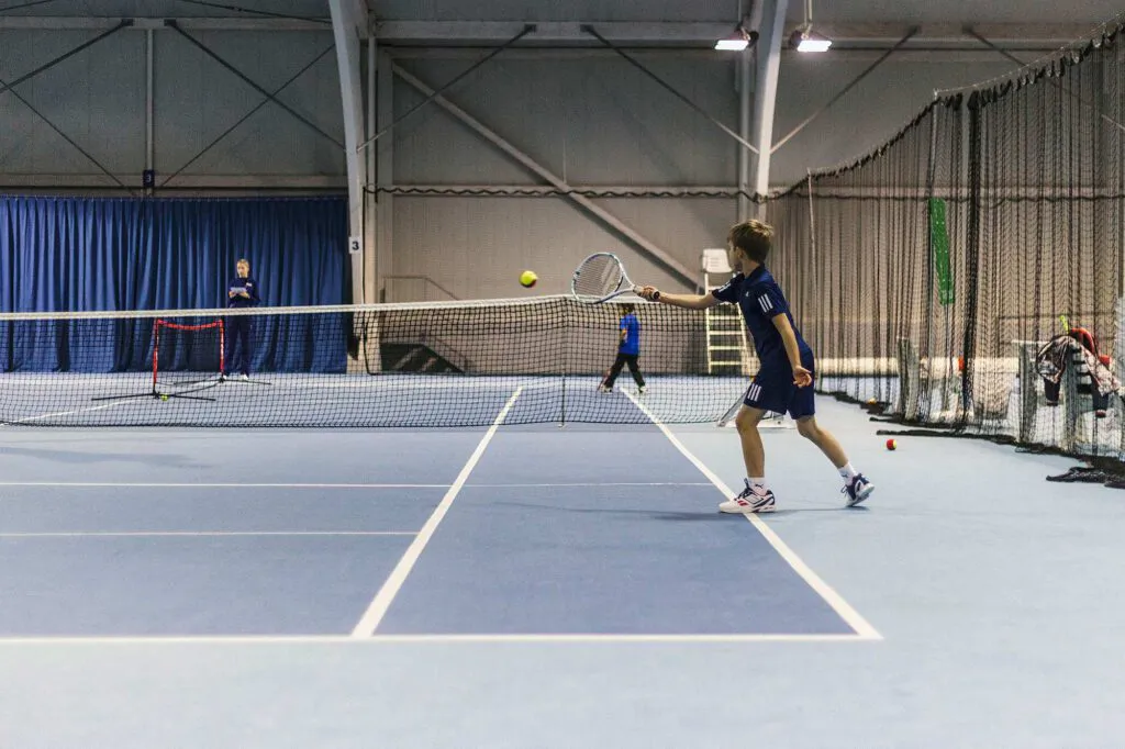 Tennisspieler schlägt einen Ball am Netz auf einem blauen Hallenplatz beim Wilson Master Cup.