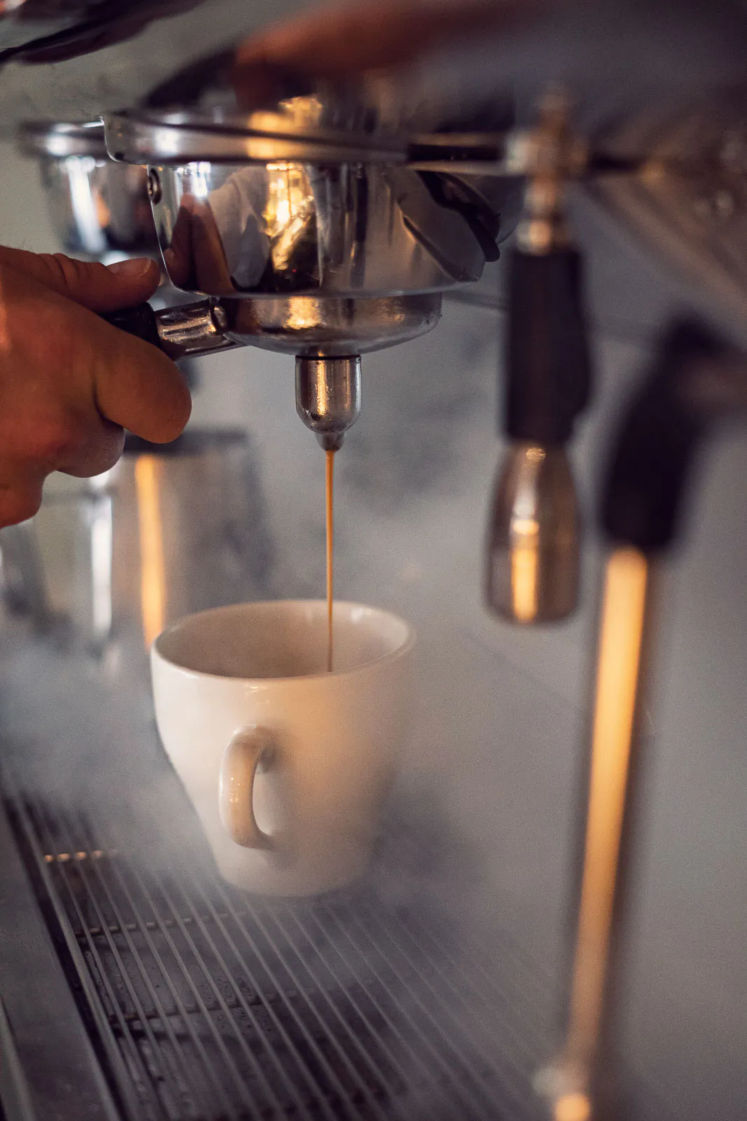Espresso fließt aus einer Siebträgermaschine in eine weiße Tasse, während eine Hand den Siebträger hält.