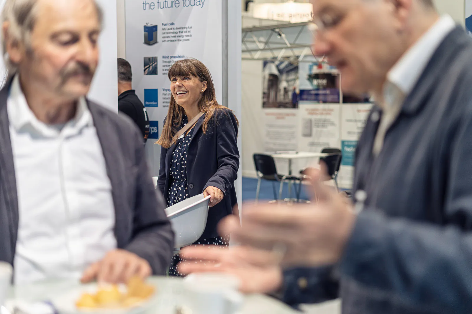 Zwei Männer im Gespräch im unscharfen Vordergrund, dahinter eine lächelnde Frau am Messestand von Alfa Laval.