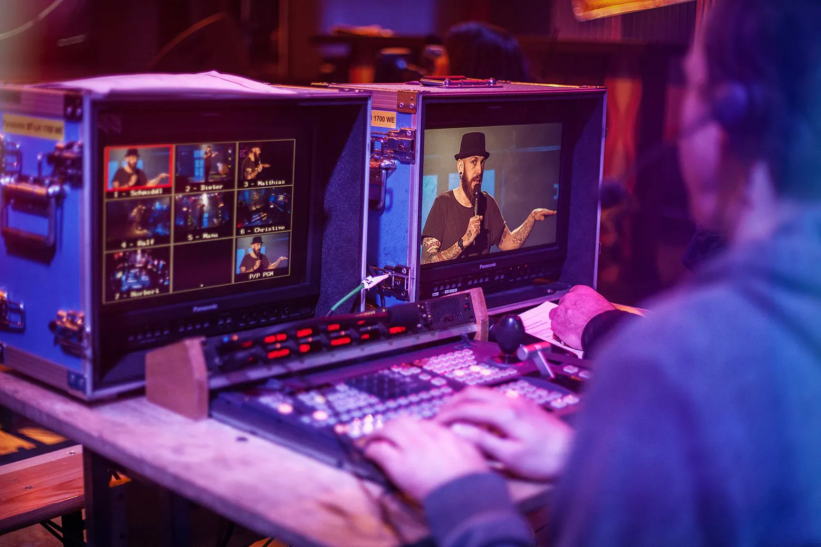 Person am Bildmischpult im violetten Regielicht, auf dem Monitor ein Comedian mit Hut und Mikrofon beim NDR Comedy Contest.