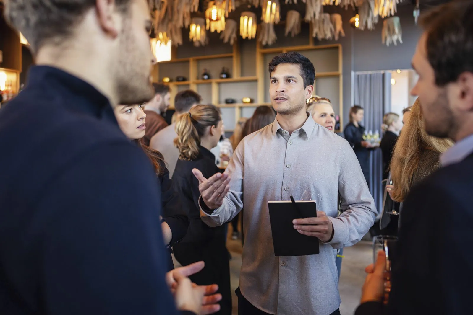 Mann mit Notizbuch gestikuliert im Gespräch mit Gästen beim Netflix-Event in warm beleuchtetem Innenraum.