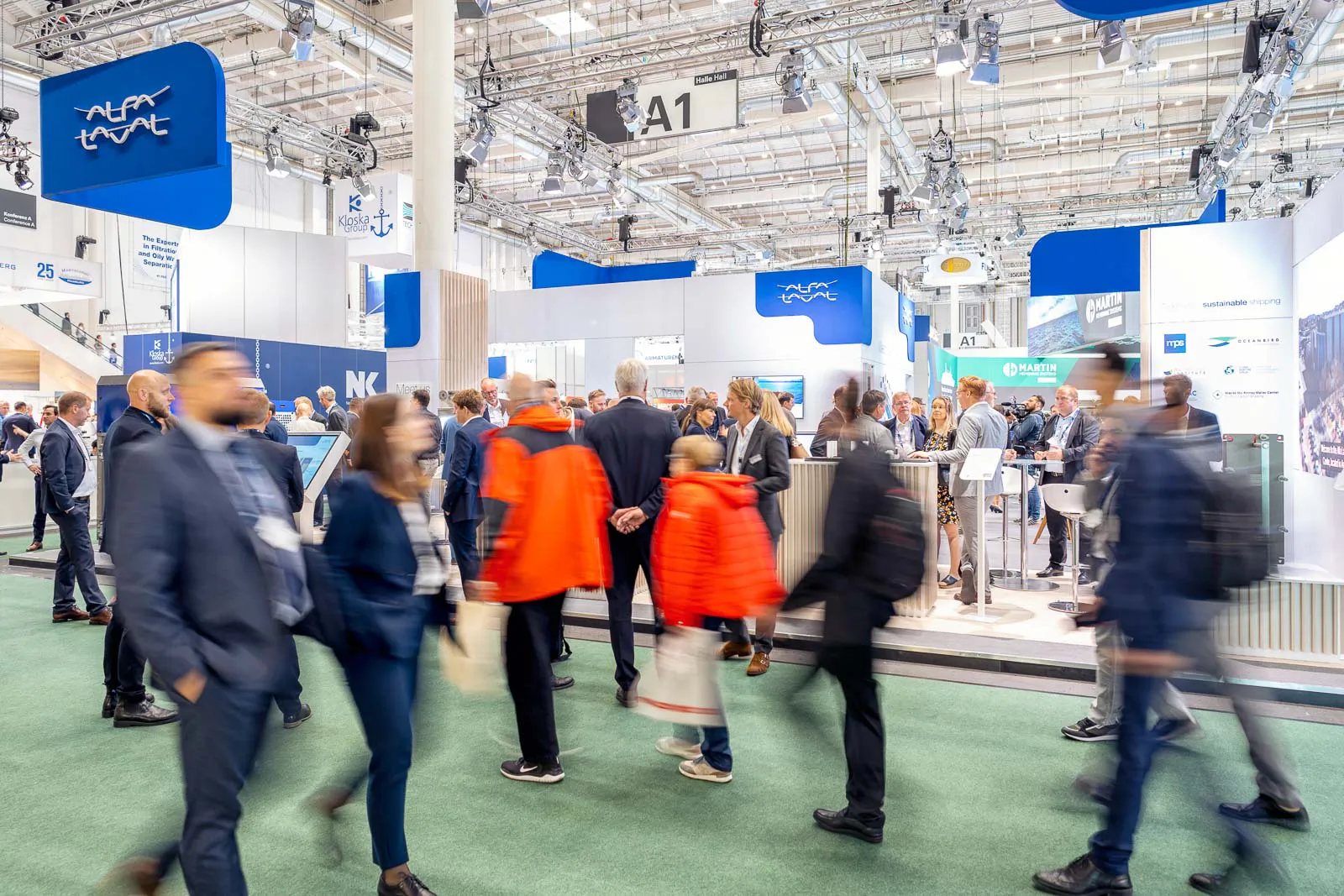Besucher gehen am blau-weißen Alfa-Laval-Messestand in einer hell beleuchteten Messehalle vorbei.