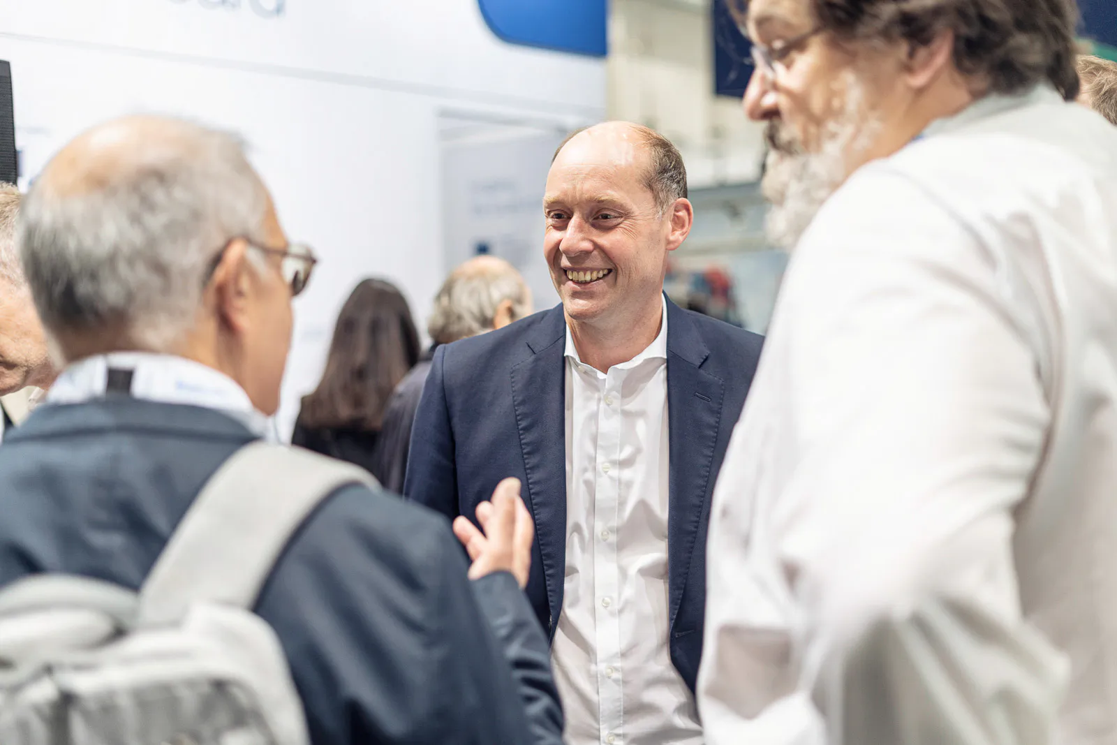 Drei Männer im Gespräch am hell beleuchteten Messestand von Alfa Laval, einer lächelt im dunklen Sakko.