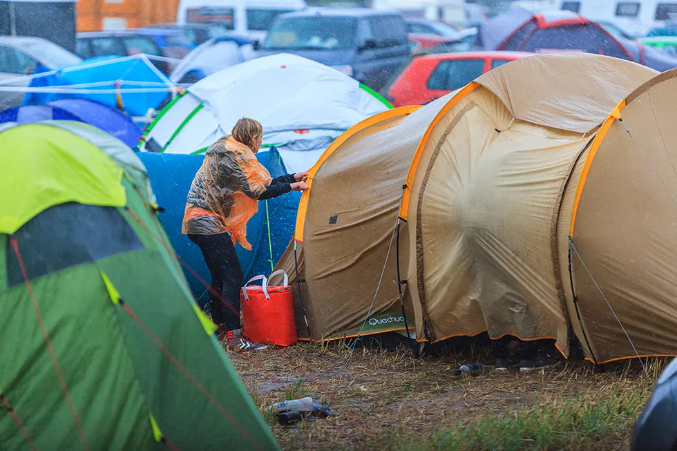 Person in gemusterter Jacke steht zwischen Zelten auf einem dicht belegten Campingplatz.