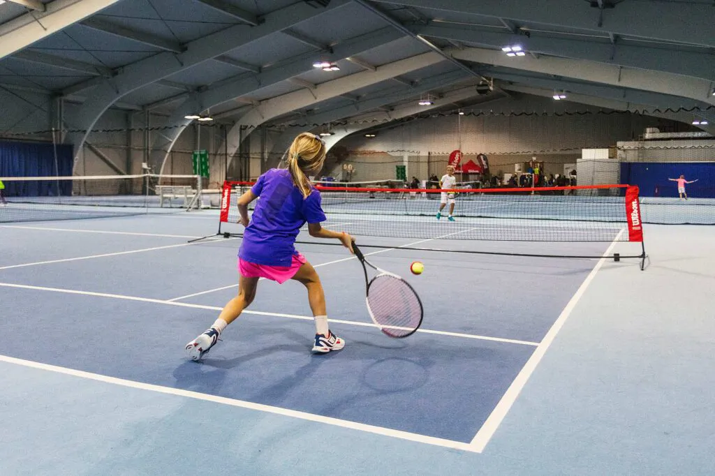 Tennisspielerin in lila Shirt und pinkem Rock schlägt einen Ball auf blauem Hallenplatz beim Wilson Master Cup.