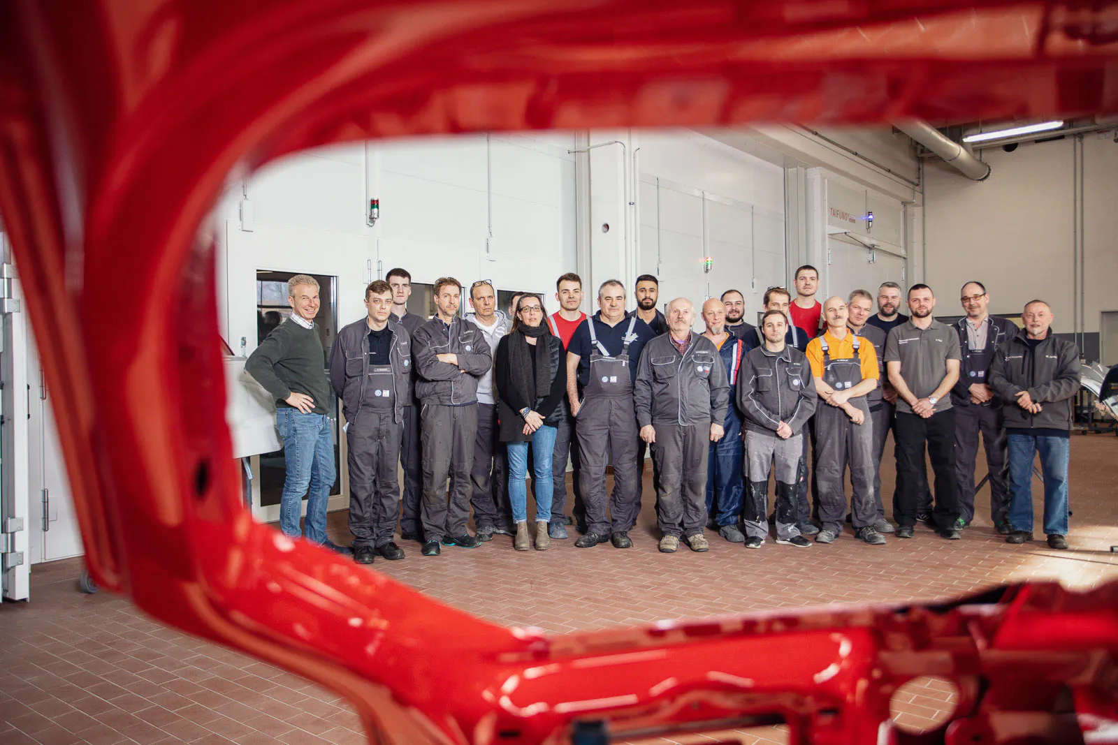 VW-Mitarbeiter posieren in einer hellen Werkhalle, eingerahmt von einer roten Autokarosserie.