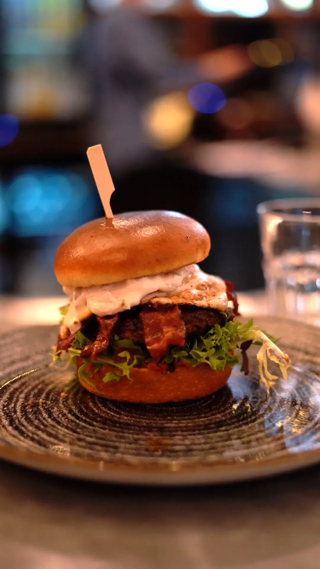 Burger mit Bacon, Spiegelei und Salat auf einem Keramikteller im warm beleuchteten Restaurant.