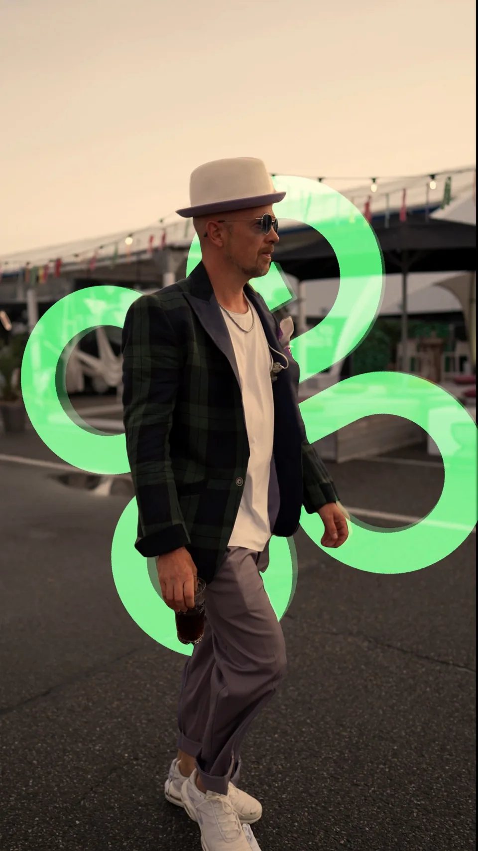 Jan Delay mit Hut, Sonnenbrille und kariertem Sakko vor einer grünen Lichtinstallation auf dem Festivalgelände.