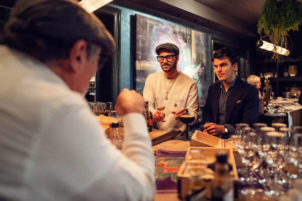 Drei Männer bei einer Botucal-Rum-Verkostung an einer warm beleuchteten Bar mit Gläsern und Flaschen.