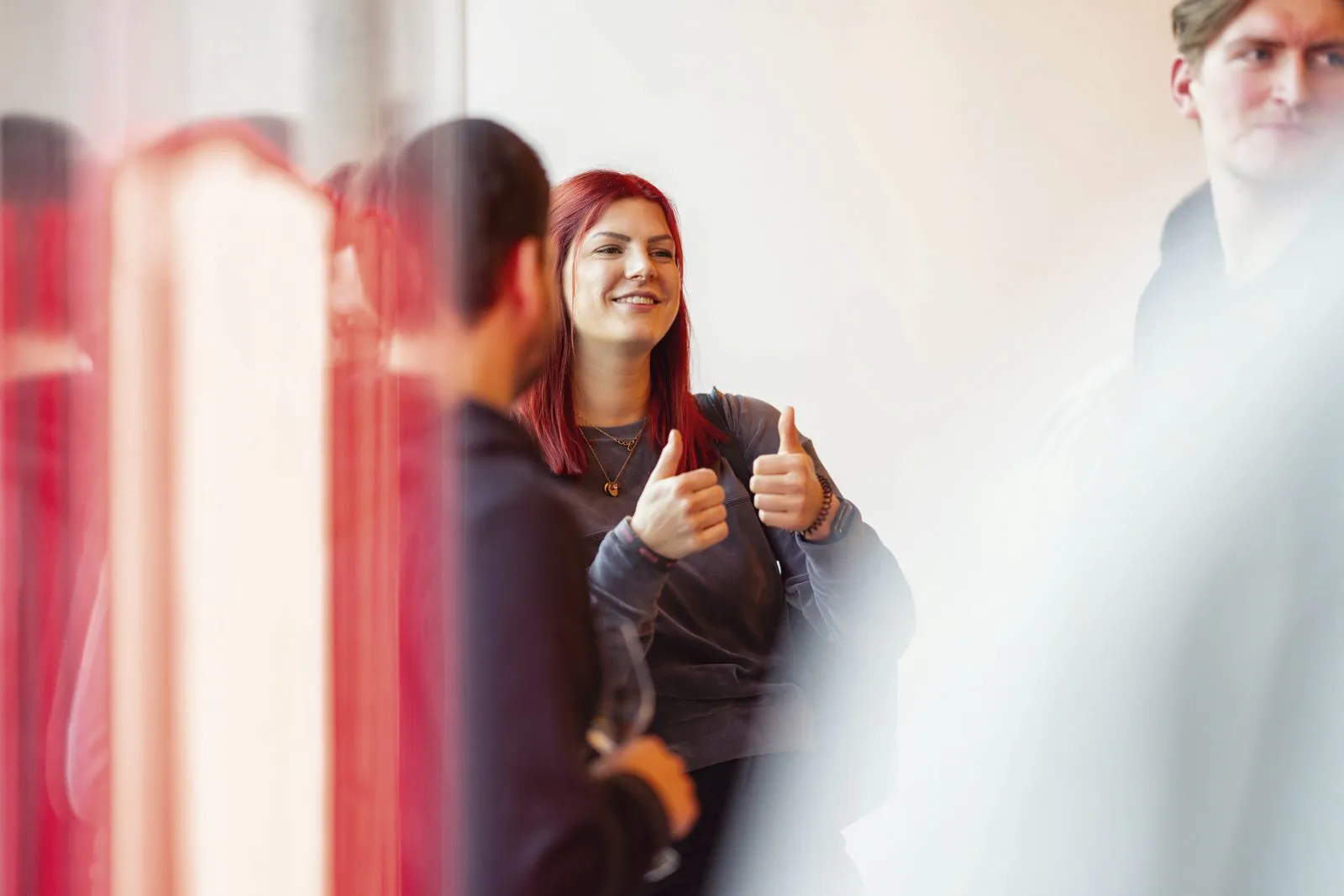 Eine lächelnde Frau hebt beide Daumen zwischen Gästen beim Netflix-Event, umgeben von roten Lichtreflexen.
