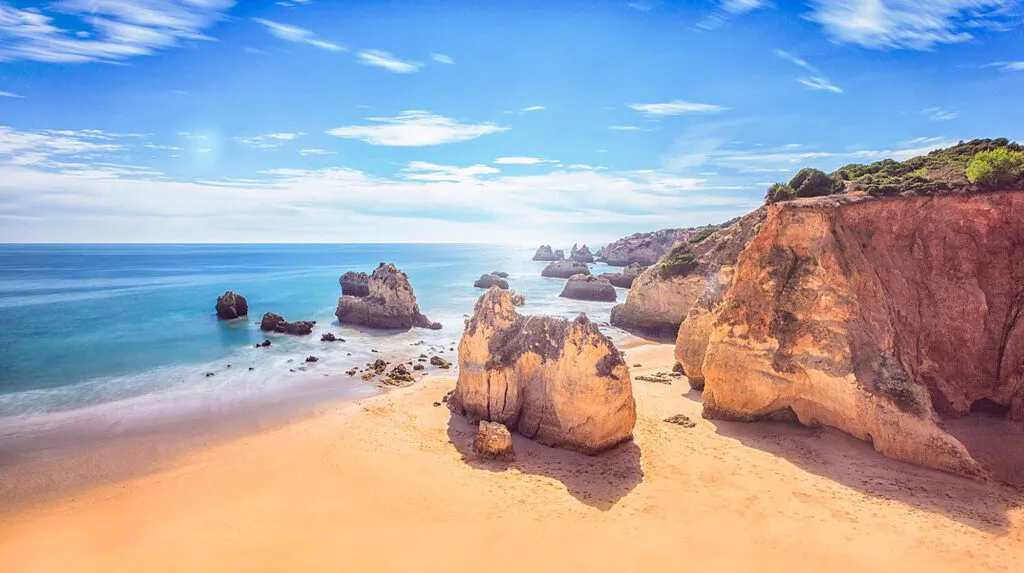 Sonniger Sandstrand an der Algarve mit goldenen Felsen, Steilküste und durch Langzeitbelichtung geglättetem Meer.