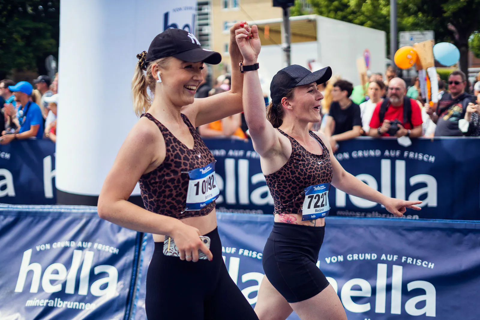 Zwei Läuferinnen im Leopardenlook halten beim Hella Halbmarathon vor Publikum jubelnd ihre Hände in die Höhe.
