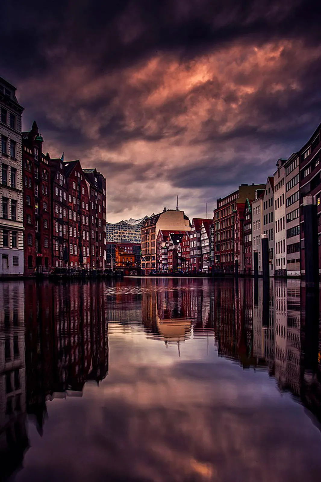 Elbphilharmonie hinter Backsteinhäusern am Fleet, gespiegelt im Wasser unter dunkelviolettem Abendhimmel.