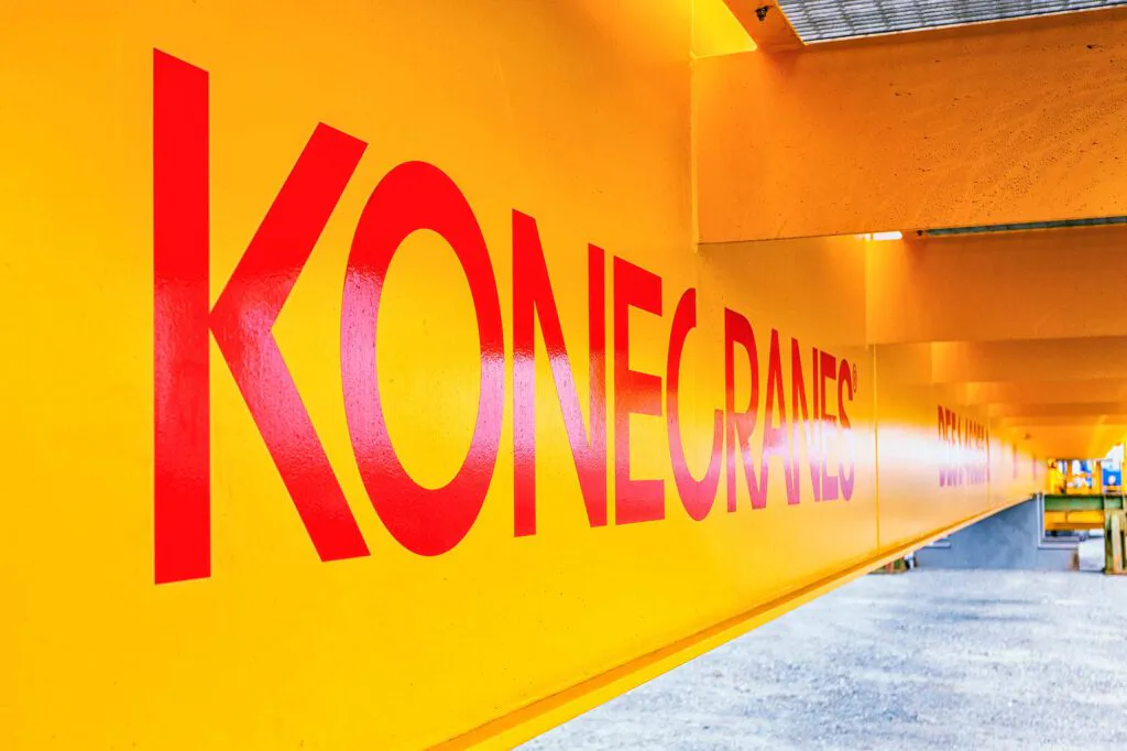 Gelber Kranträger mit rotem Konecranes-Schriftzug in einer hell beleuchteten Industriehalle.