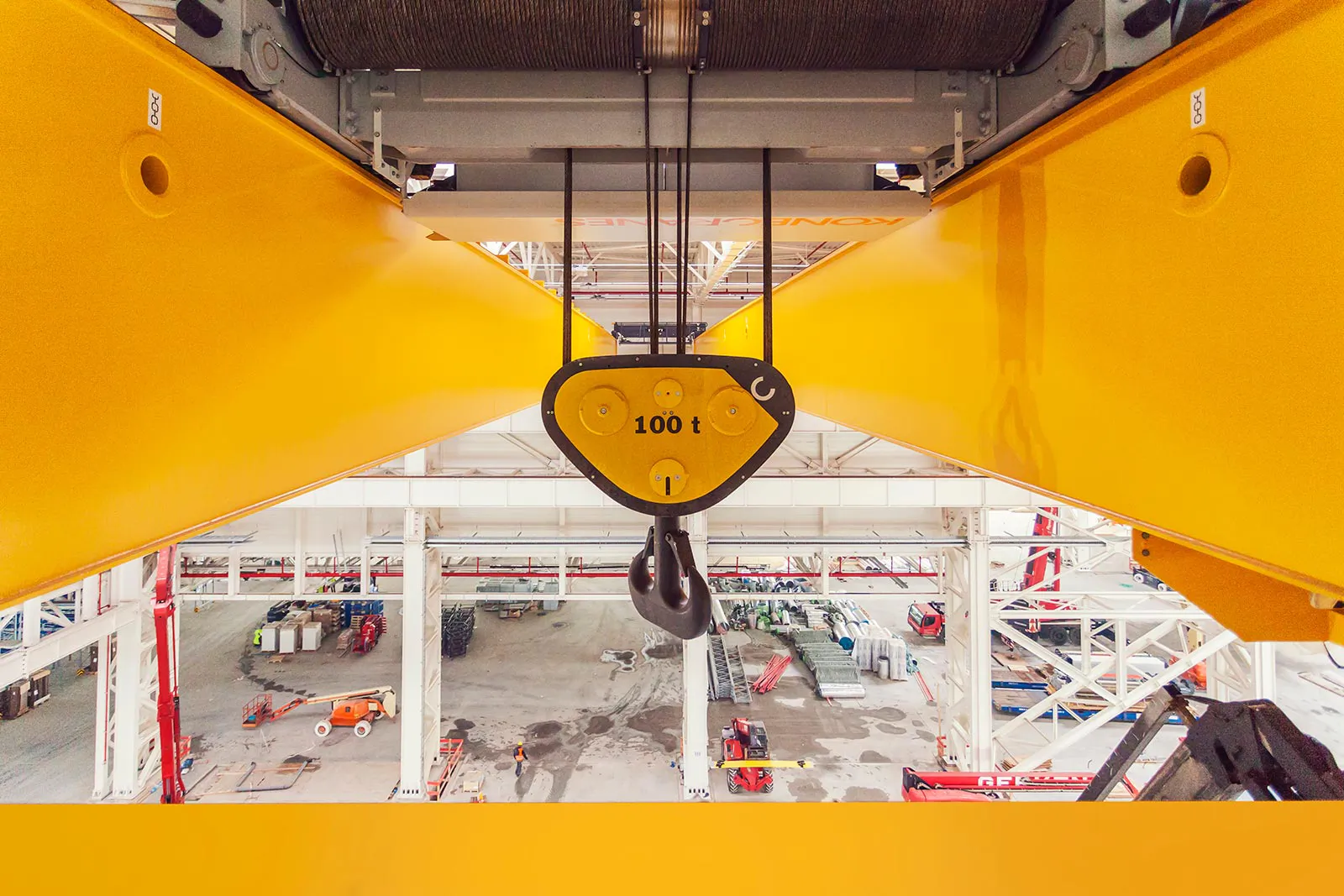 100-Tonnen-Kranhaken zwischen gelben Kranträgern über der Montagefläche einer hellen Industriehalle.
