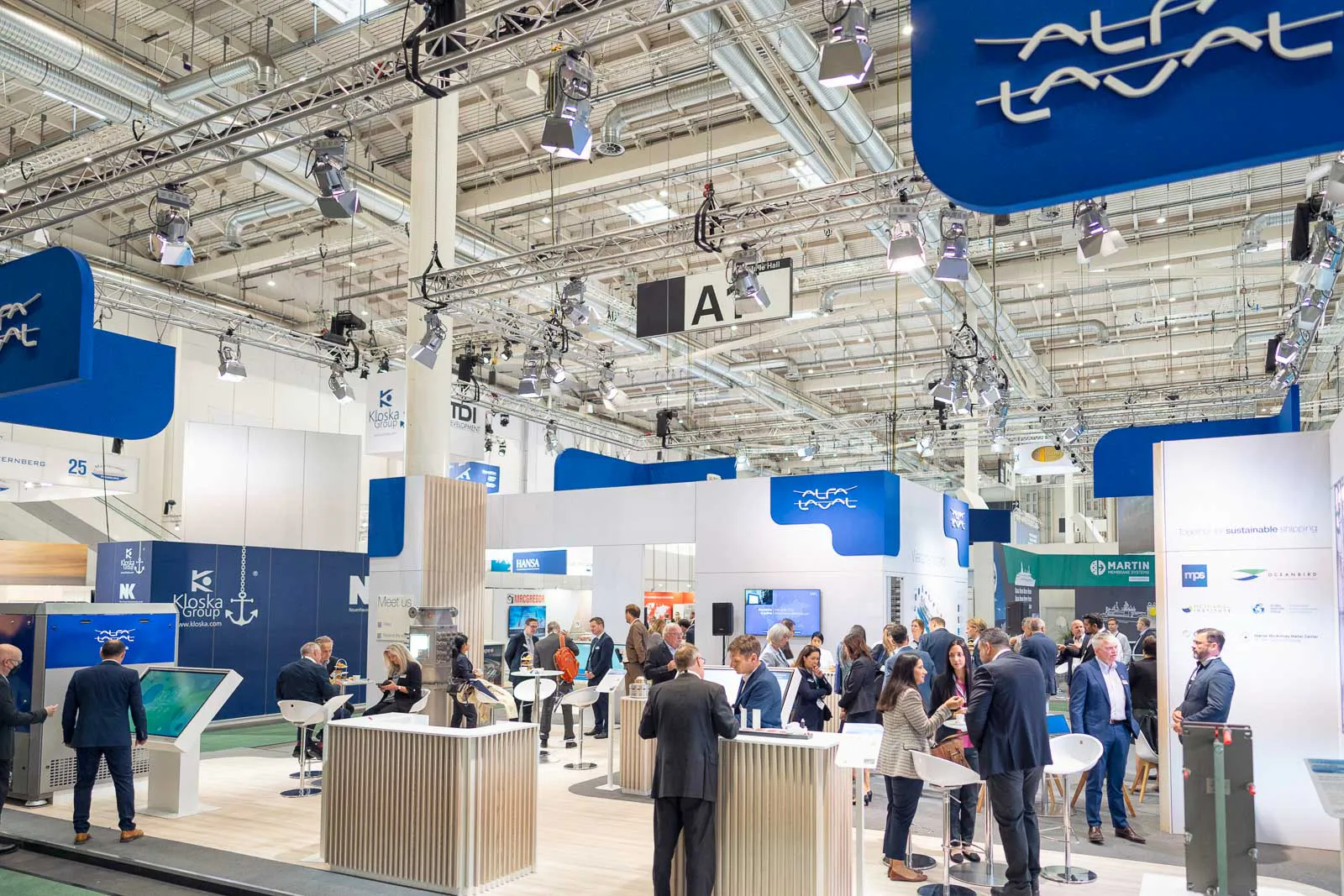 Besucher im Gespräch an Stehtischen am hell beleuchteten Alfa-Laval-Messestand in einer großen Halle.