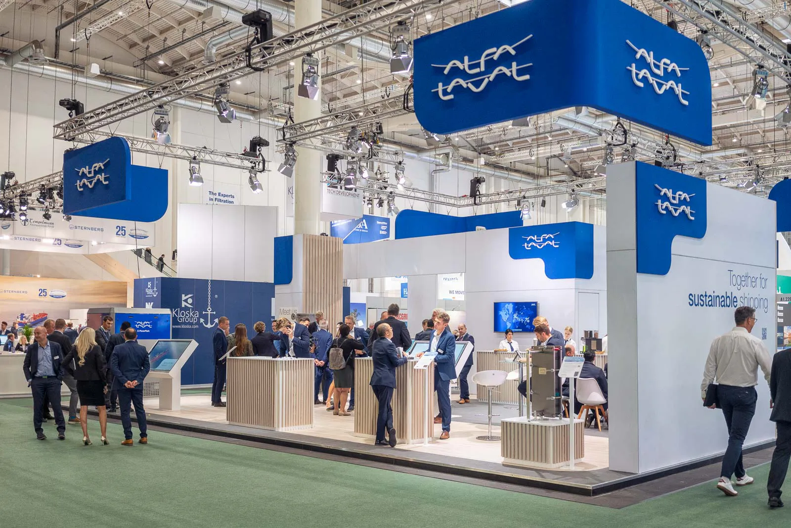 Besucher im Gespräch am hell beleuchteten Alfa-Laval-Messestand mit blau-weißen Logos und technischen Exponaten.
