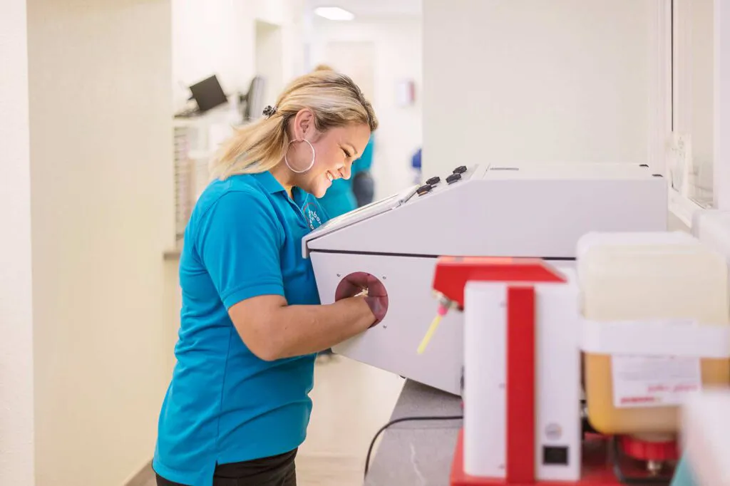 Eine Frau im türkisfarbenen Poloshirt arbeitet an einem geschlossenen Laborgerät im hellen Dental-Labor Ralf Gaida.