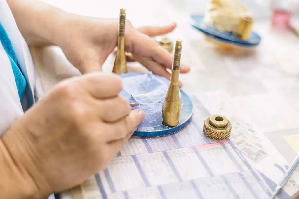 Hände arbeiten an einem Modell mit goldfarbenen Stiften auf einer blauen Unterlage im Dental-Labor Ralf Gaida.