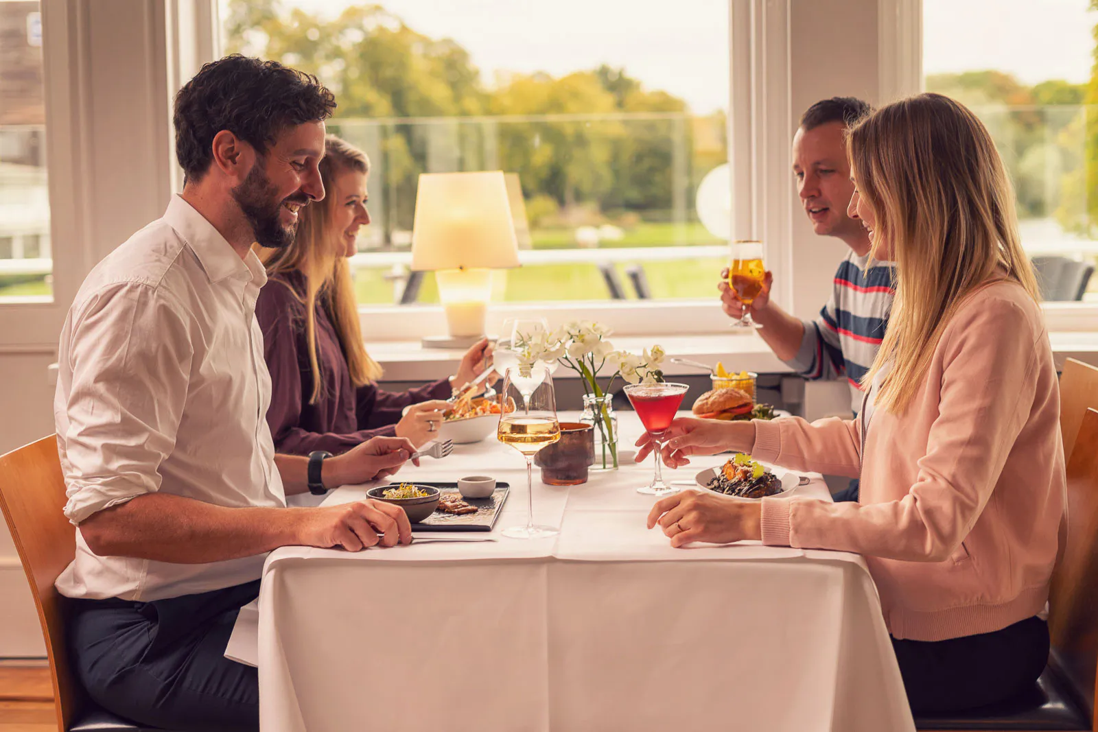 Vier Personen essen und trinken an einem weiß gedeckten Tisch im hellen Restaurant des Insel Beach Club Hannover.