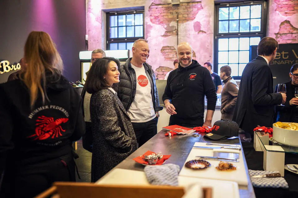 Gäste unterhalten sich am Hummer-Pedersen-Stand mit Meeresfrüchten vor einer pink beleuchteten Backsteinwand.