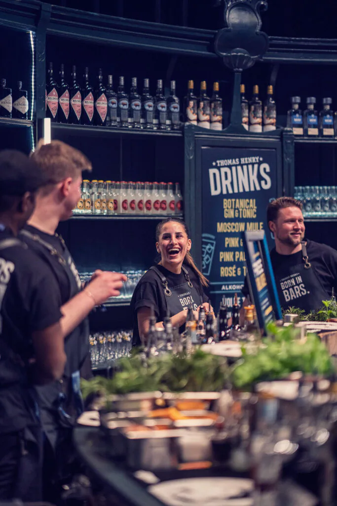 Barteam am Tresen mit Kräutern und Flaschen vor einem Thomas-Henry-Drinks-Schild beim OMR Festival.